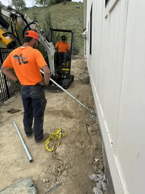 Crew installing a helical tieback anchor outside a home