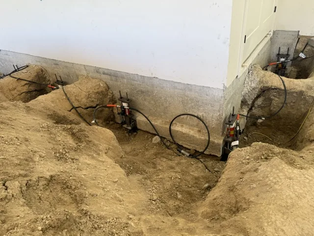 Hydraulic push pier drive heads clamped along a concrete foundation wall during installation